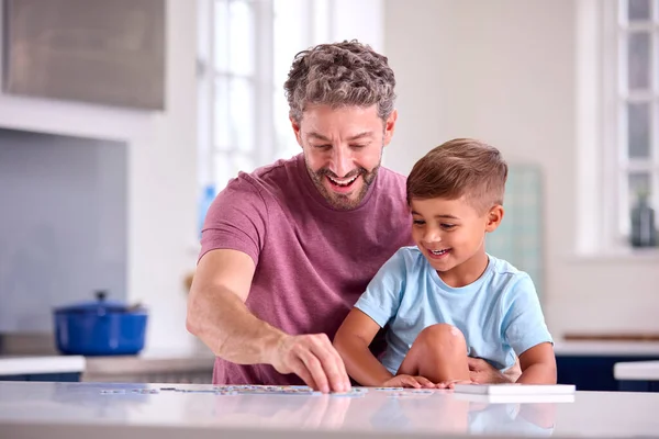 息子と一緒にジグソーパズルをやってキッチンで自宅で成熟したお父さん — ストック写真