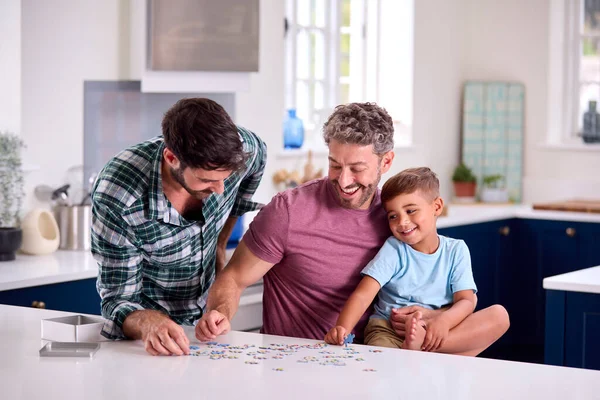 两个爸爸的同性家庭和儿子在家里厨房里玩拼图游戏 — 图库照片
