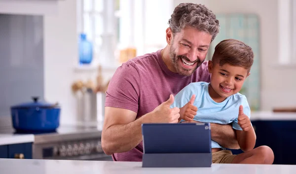 デジタルタブレットでビデオ通話をする息子とキッチンで自宅で成熟したお父さん — ストック写真