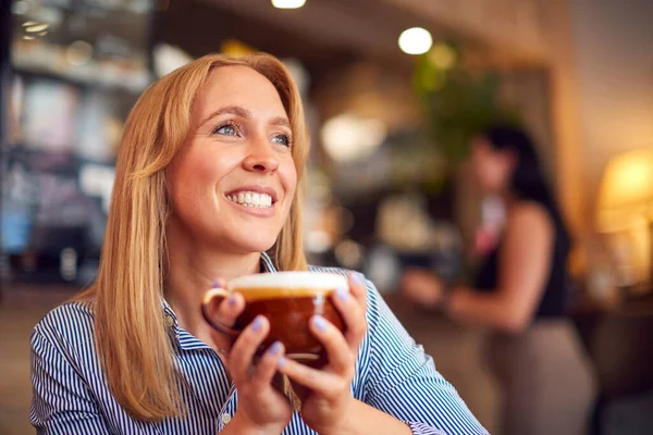 コーヒーショップのテーブル席に座る笑顔の女性が熱い飲み物を楽しむ — ストック写真