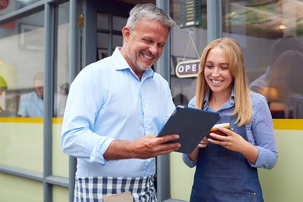 デジタルタブレットを見てコーヒーショップの外に立つ男性と女性のオーナーやスタッフ — ストック写真