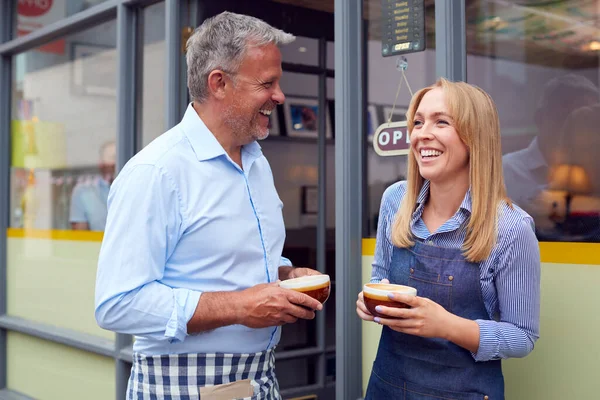 男性と女性のオーナーやスタッフがコーヒーショップの外に立ち熱い飲み物を持っている — ストック写真