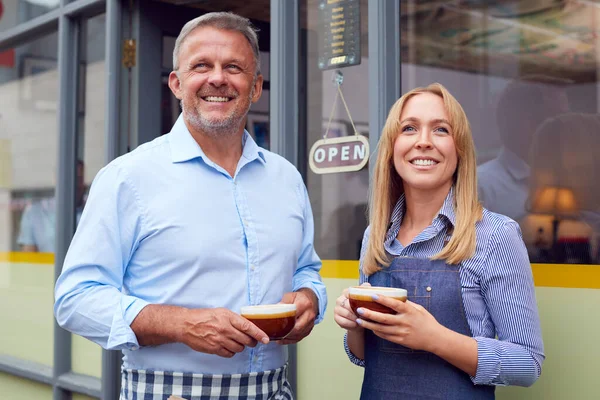 男性と女性のオーナーやスタッフがコーヒーショップの外に立ち熱い飲み物を持っている — ストック写真