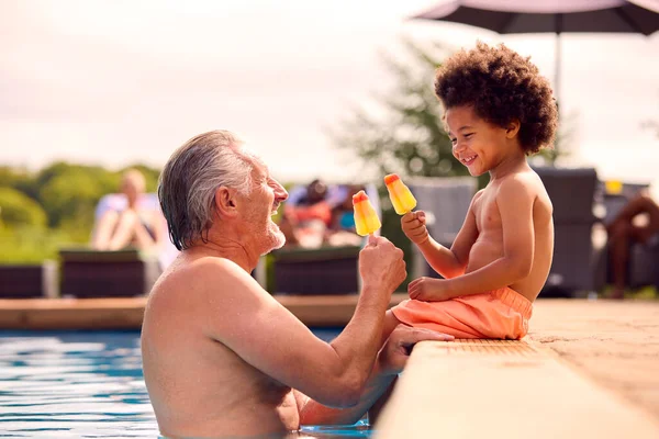 祖父と孫は夏休みにプールの端でアイスロリーを食べる — ストック写真