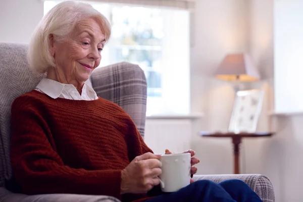 坐在家中客厅扶手椅上热饮的老年妇女 — 图库照片