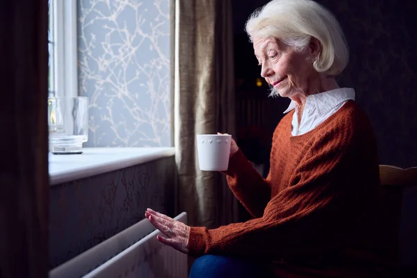Senior Kvinna Med Varm Dryck Försöker Hålla Värmen Genom Radiator — Stockfoto