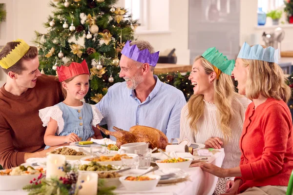 一緒に食事をする前に紙の帽子をかぶって家でクリスマスを祝う世代の家族 — ストック写真