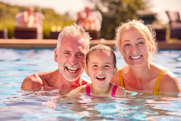 祖父母の肖像プールで家族の夏休みに泳ぐ孫娘を教える — ストック写真