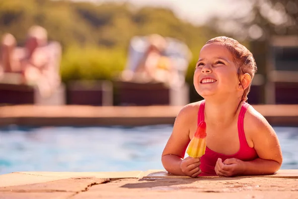 プールの端でアイスロリーを食べる女の子と夏休みの家族 — ストック写真