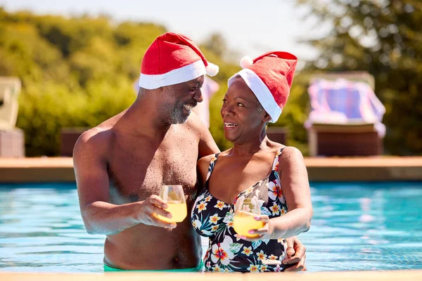 资深情侣在圣诞假期穿著圣诞老人帽在游泳池游泳 — 图库照片