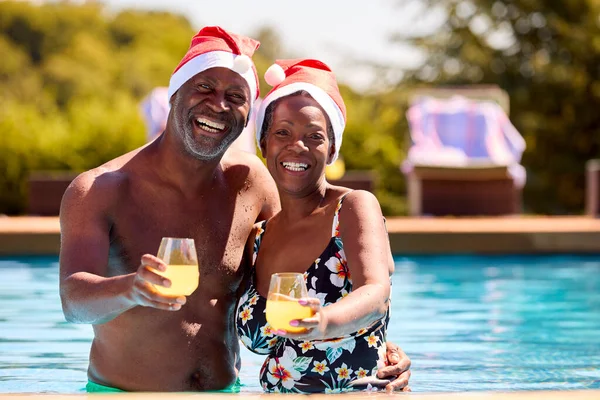 サンタの帽子をかぶってスイミングプールでのクリスマス休暇中のシニアカップルの肖像 — ストック写真