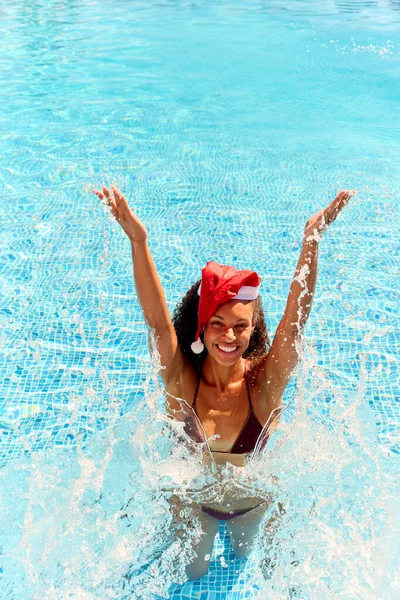 圣诞假期里穿着圣诞老人帽在游泳池里飞溅的女人的画像 — 图库照片