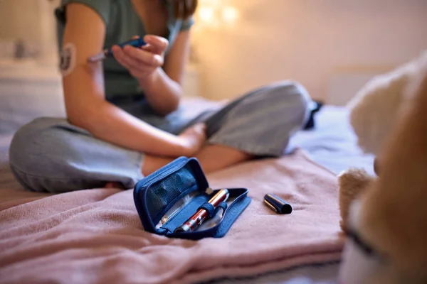 自宅のベッドルームでベッドに座っている若い糖尿病の女の子のクローズアップキットを使用してインスリンレベルを確認します — ストック写真