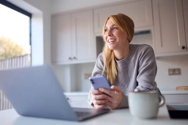 Kadın Evde Cep Telefonu Yulaflı Dizüstü Bilgisayarla Mutfakta Çalışıyor — Stok fotoğraf