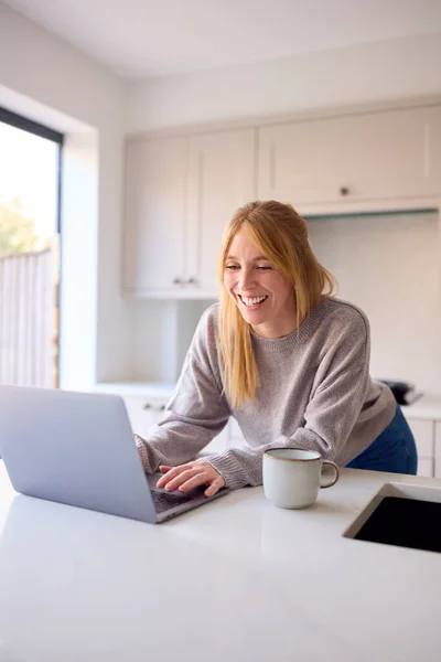 Woman At Home Working On Laptop On Counter In Kitchen