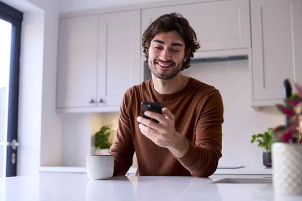 Mutfakta Dinlenen Genç Adam Cep Telefonu Kullanarak Sıcak Içecek Tutuyor — Stok fotoğraf