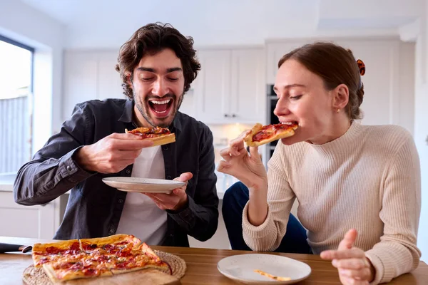 厨房里的夫妇在家吃自制的比萨坐在柜台边 — 图库照片