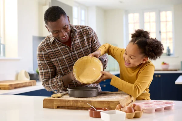 父と娘と一緒に家で焼くキッチンでケーキの混合物を注ぎます錫 — ストック写真
