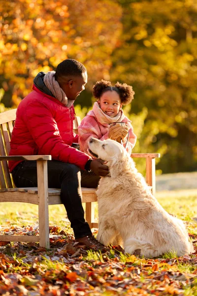 秋の田舎を歩くペット犬とベンチに座って熱い飲み物を持つ父と娘 — ストック写真