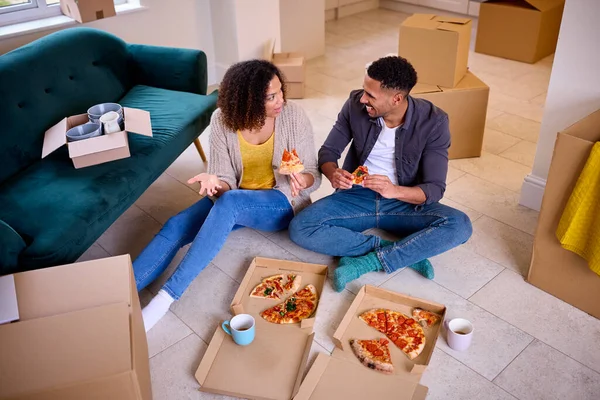 Excited Couple Moving Into New Home Celebrating Sitting On Floor Eating Takeaway Pizza