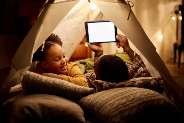 Father And Daughter At Home Lying In Indoor Tent Or Camp Watching Or Streaming To Digital Tablet