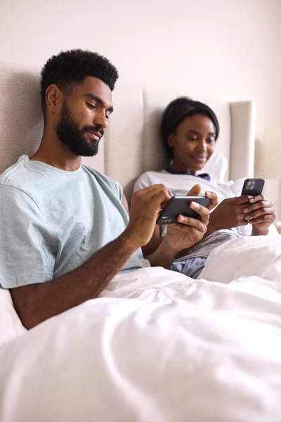 若いカップルが家で一緒にベッドで携帯電話を見て — ストック写真