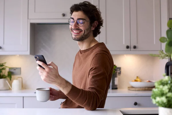 Mutfakta Dinlenen Genç Adam Cep Telefonu Kullanarak Sıcak Içecek Tutuyor — Stok fotoğraf