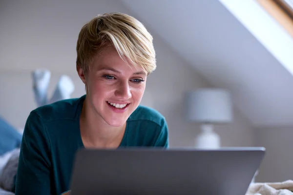 Yatağında Pijamalarıyla Dizüstü Bilgisayar Başında Oturan Gülümseyen Genç Bir Kadın — Stok fotoğraf