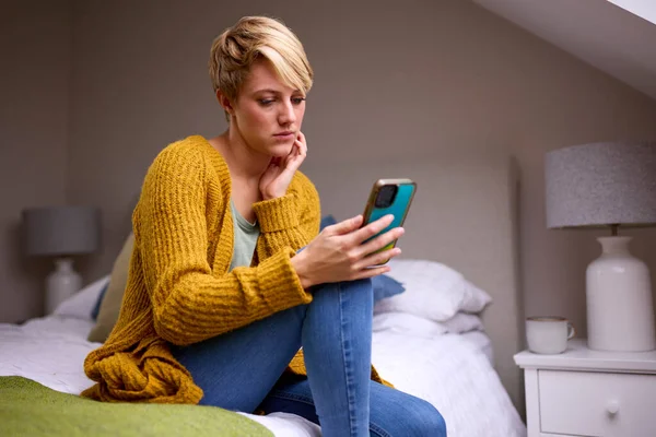 Olycklig Ung Kvinna Sitter Sängen Hemma Tittar Mobiltelefon — Stockfoto