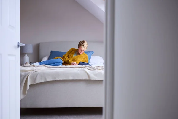 自宅でベッドに寝そべっている若い女性の扉を通して見るデジタルタブレット — ストック写真