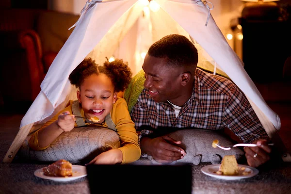 屋内テントに寝そべっている父と娘 またはデジタルタブレットでキャンプ一緒にケーキを食べる — ストック写真