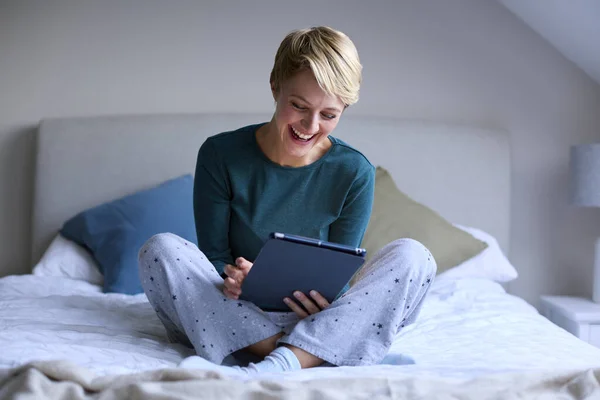 Yatağında Pijamalarıyla Oturup Dijital Tablete Bakan Gülümseyen Genç Bir Kadın — Stok fotoğraf