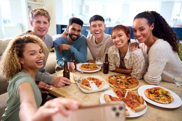 友達は自宅で楽しんでいる電話でセルフィーを取るキッチンで自家製ピザを食べる — ストック写真
