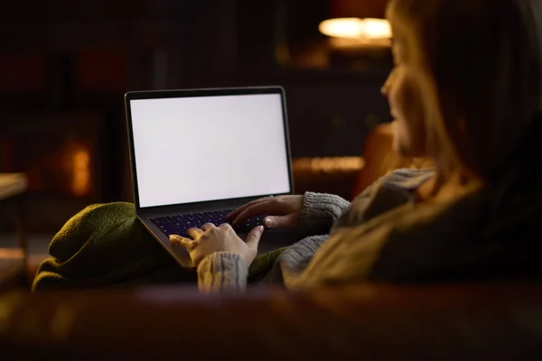 在客厅里的女人躺在沙发上 炉火熊熊地望着笔记本电脑上的空白屏风 — 图库照片