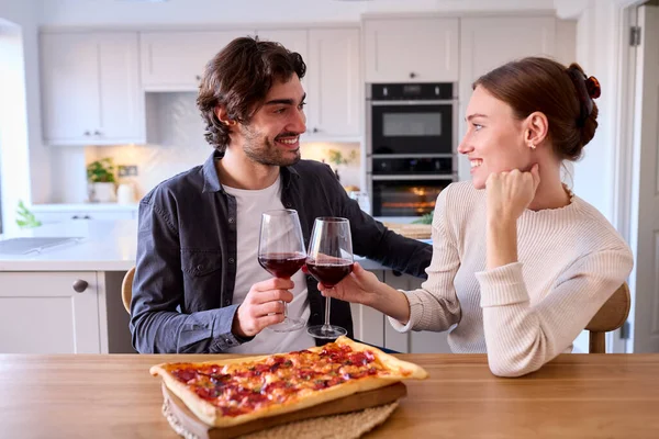 厨房里的一对夫妇在家吃自制的比萨 坐在柜台边喝酒 — 图库照片