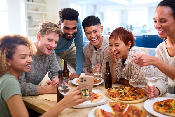 友達は自宅で楽しんでいる電話でセルフィーを取るキッチンで自家製ピザを食べる — ストック写真