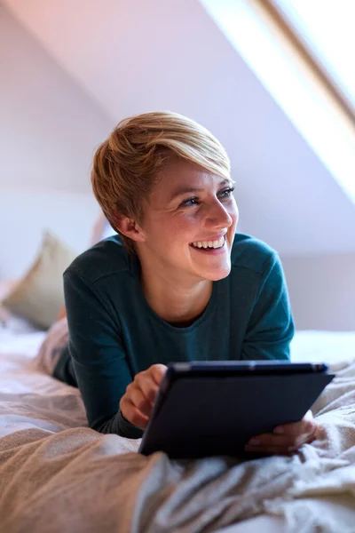 Evde Pijamalarıyla Yatıp Dijital Tablete Bakan Gülümseyen Genç Bir Kadın — Stok fotoğraf