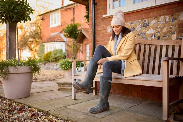 家の外のベンチに座っている女性秋の散歩の準備ができてブーツを着る — ストック写真