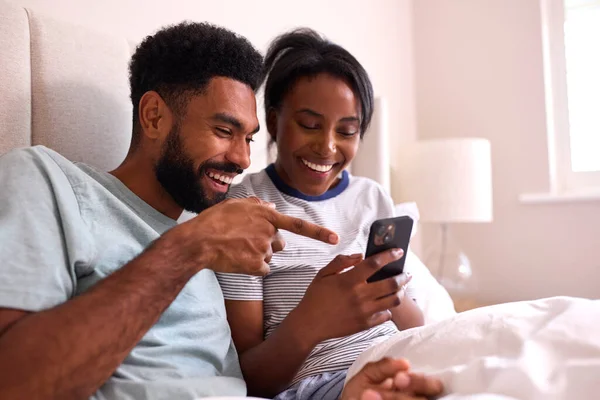 一对年轻夫妇在家里 两个人在床上一起看手机 — 图库照片