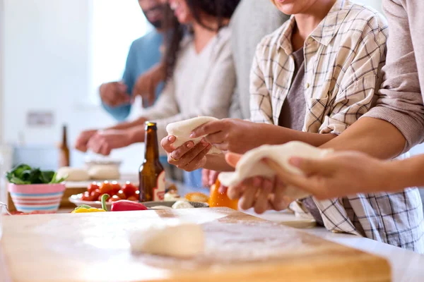 Close Up Of Group Of Friends At Home In Kitchen With Making Pizzas For Party Together