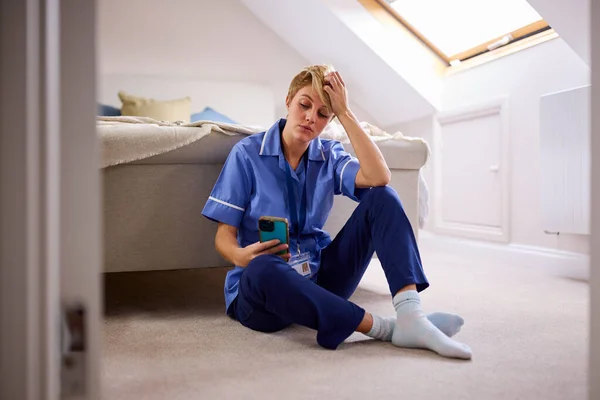 头脑清醒的女人穿着护士或医生制服坐在地板上看手机 — 图库照片