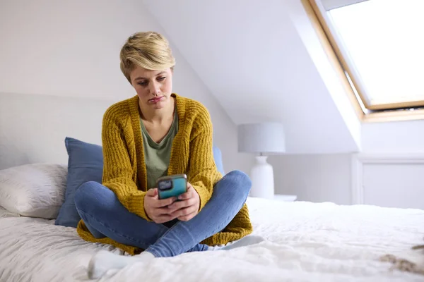 Нещаслива Молода Жінка Сидить Ліжку Вдома Дивлячись Мобільний Телефон — стокове фото