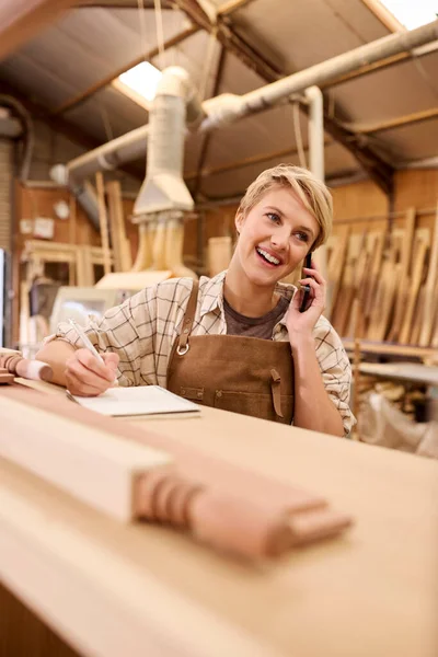 家具ワークショップの大工として働く女性の見習い電話をかける — ストック写真