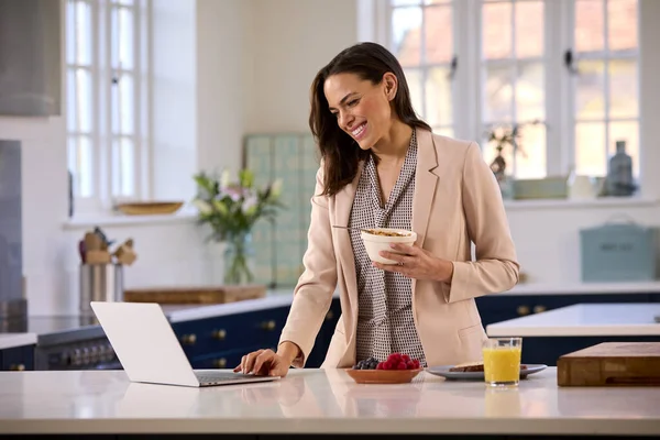 带着手提电脑在厨房柜台边吃饭的女商人下班前吃早餐 — 图库照片