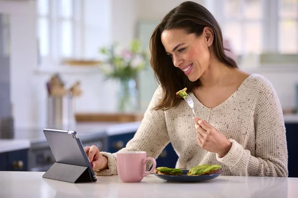 自宅でデジタルタブレットでキッチンカウンターで昼食を食べる女性 — ストック写真