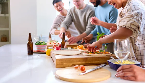 Skupina Přátel Doma Kuchyni Přidávání Polevy Domácí Pizzy Pro Párty — Stock fotografie