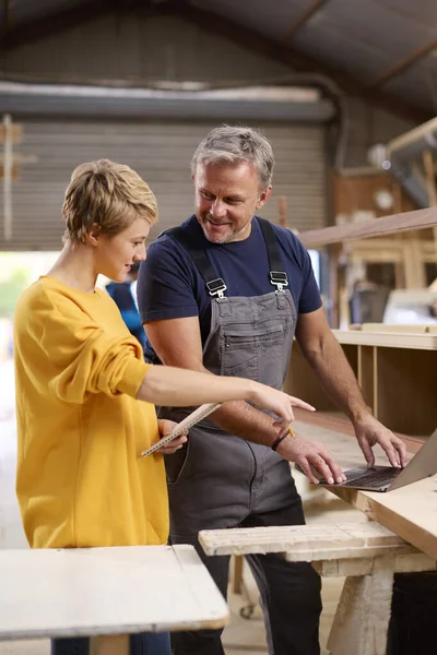 Female Apprentice Learning Skills From Mature Male Carpenter In Furniture Workshop