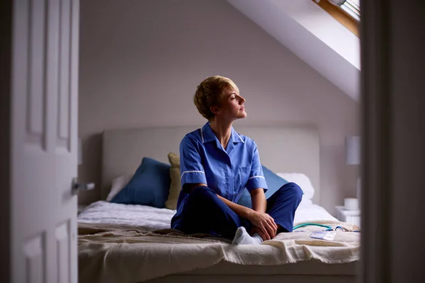 Bedachtzame Vrouw Draagt Verpleegsters Artsen Uniform Zittend Bed Thuis — Stockfoto