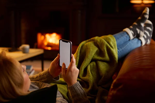 在家躺在沙发上的女人用空白屏风手机躺在有余火的客厅里 — 图库照片