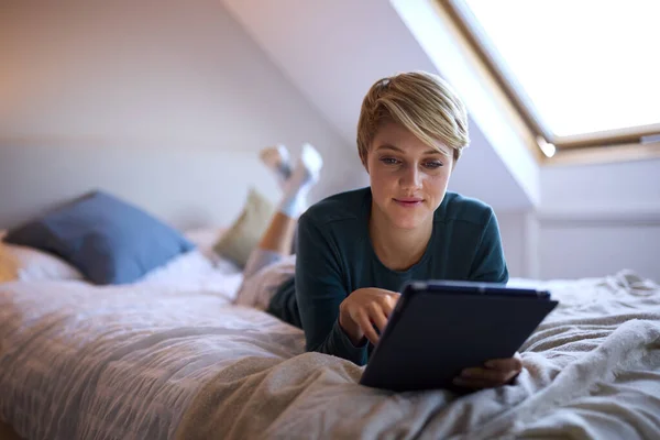 自宅でパジャマを着てベッドに寝そべっている若い女性デジタルタブレットを見て — ストック写真